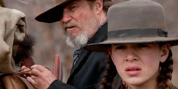 Rooster Cogburn attachant son sac, debout à côté de Mattie Ross